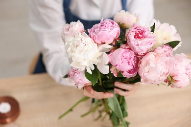 Photo of Florist with beautiful bouquet of peonies at table, above view