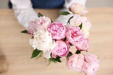 Photo of Florist with beautiful bouquet of peonies at table, top view