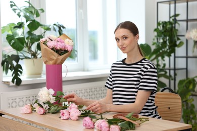 Photo of Florist making bouquet of peonies at wooden table in flower shop