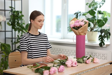 Photo of Florist making bouquet of peonies at wooden table in flower shop