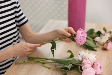 Photo of Florist making bouquet of peonies at wooden table in flower shop, closeup