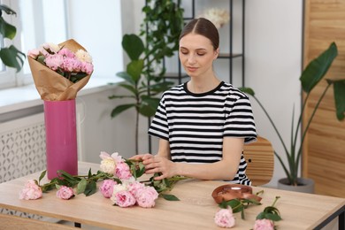 Photo of Florist making bouquet of peonies at wooden table in flower shop