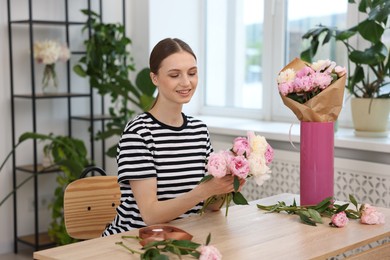 Photo of Florist making bouquet of peonies at wooden table in flower shop