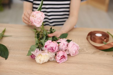 Photo of Florist making bouquet of peonies at wooden table in flower shop, closeup