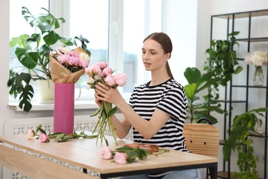 Photo of Florist making bouquet of peonies at wooden table in flower shop