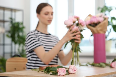 Photo of Florist making bouquet of peonies at table in flower shop, selective focus