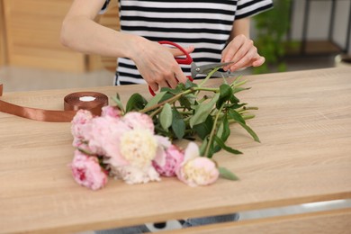 Photo of Florist making bouquet of peonies at wooden table in flower shop, closeup