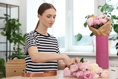 Photo of Florist making bouquet of peonies at table in flower shop