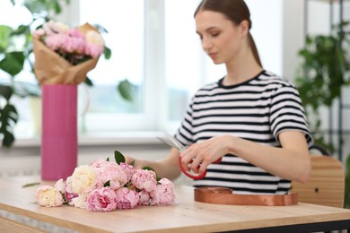 Photo of Florist making bouquet of peonies at table in flower shop, selective focus
