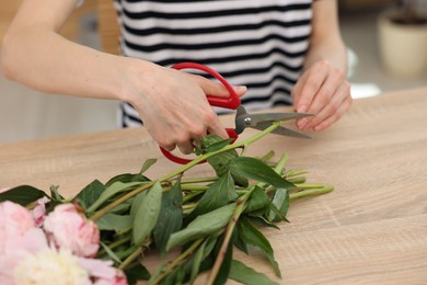 Photo of Florist making bouquet of peonies at wooden table in flower shop, closeup