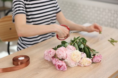 Photo of Florist making bouquet of peonies at wooden table in flower shop, closeup