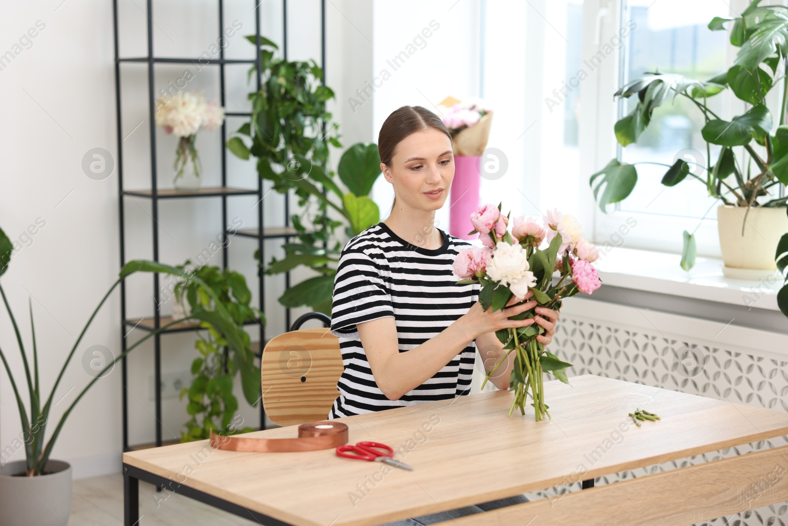 Florist making bouquet of peonies at wooden table in flower shop Photo of Florist making bouquet of peonies at wooden table in flower shop