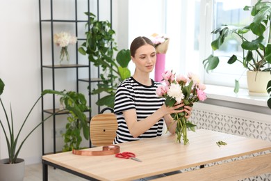 Photo of Florist making bouquet of peonies at wooden table in flower shop