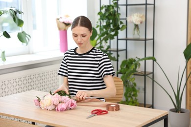 Photo of Florist making bouquet of peonies at wooden table in flower shop