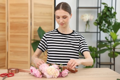 Photo of Florist making bouquet of peonies at wooden table in flower shop