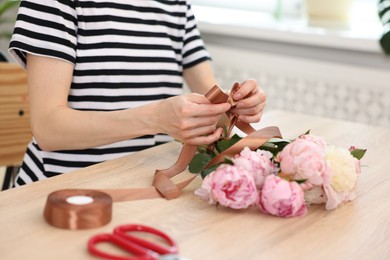 Photo of Florist making bouquet of peonies at wooden table in flower shop, closeup
