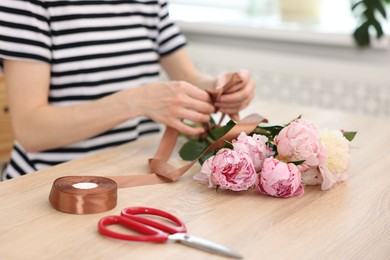 Photo of Florist making bouquet of peonies at wooden table in flower shop, selective focus