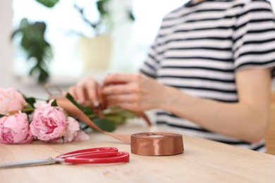 Photo of Florist making bouquet of peonies at wooden table in flower shop, selective focus