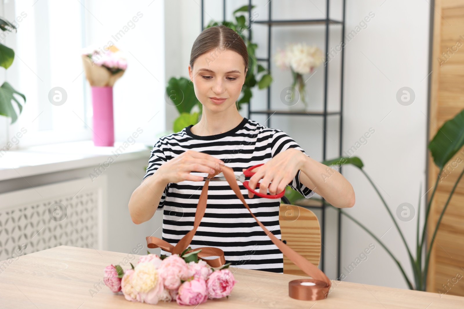 Florist making bouquet of peonies at wooden table in flower shop Photo of Florist making bouquet of peonies at wooden table in flower shop