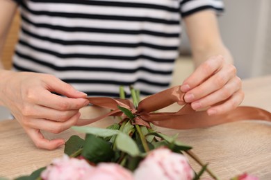 Photo of Florist making bouquet of peonies at wooden table in flower shop, closeup