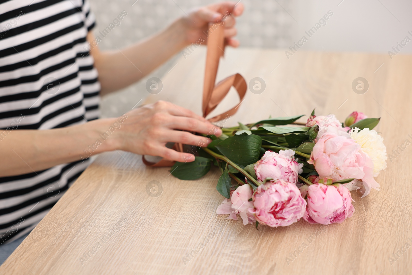 Florist making bouquet of peonies at wooden table in flower shop, closeup Photo of Florist making bouquet of peonies at wooden table in flower shop, closeup