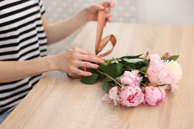 Photo of Florist making bouquet of peonies at wooden table in flower shop, closeup