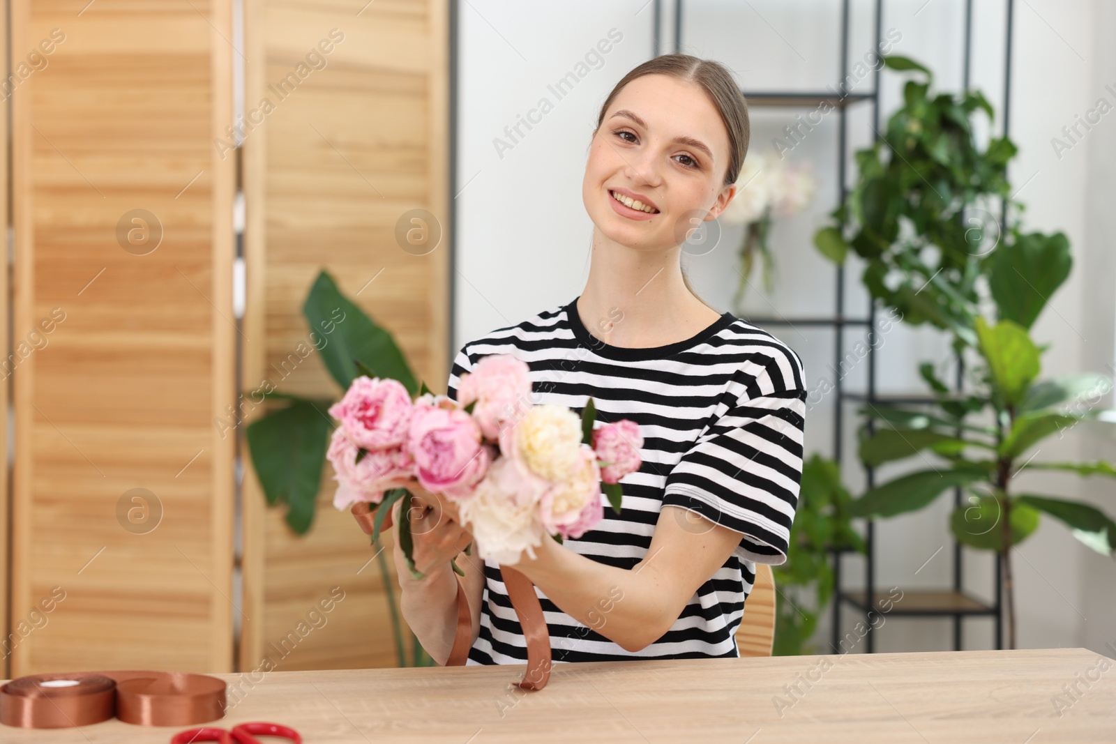 Florist with bouquet of peonies at wooden table in flower shop Photo of Florist with bouquet of peonies at wooden table in flower shop