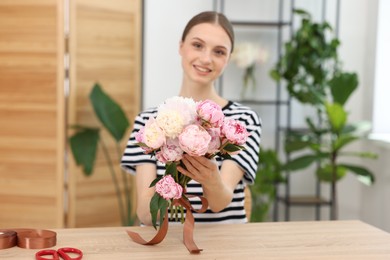 Photo of Florist with bouquet of peonies at wooden table in flower shop, selective focus