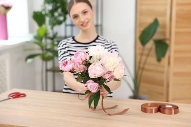 Photo of Florist with bouquet of peonies at wooden table in flower shop, selective focus