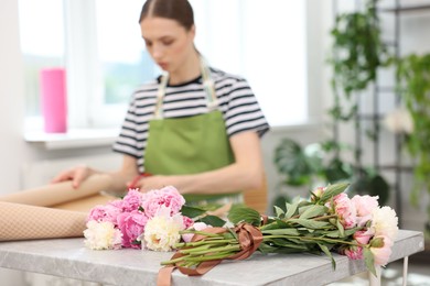 Photo of Florist making bouquet of peonies at table in flower shop, selective focus
