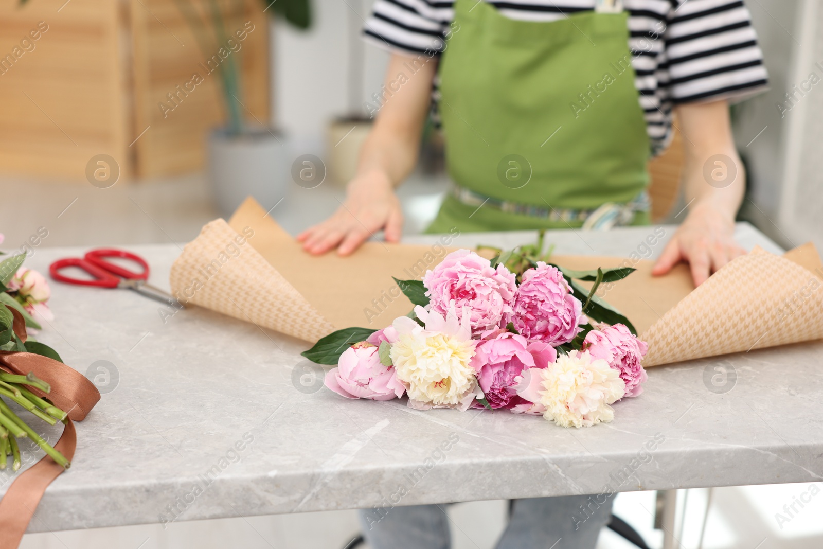 Florist making bouquet of peonies at grey marble table in flower shop, closeup Photo of Florist making bouquet of peonies at grey marble table in flower shop, closeup