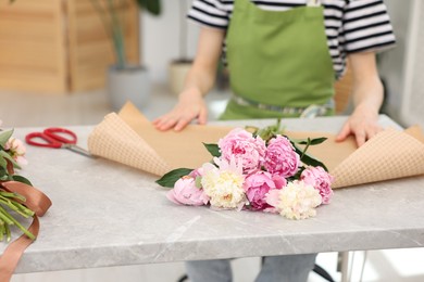 Photo of Florist making bouquet of peonies at grey marble table in flower shop, closeup