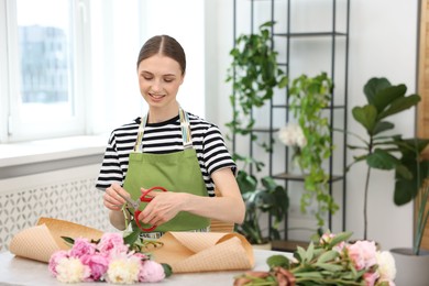 Photo of Florist making bouquet of peonies at table in flower shop, space for text