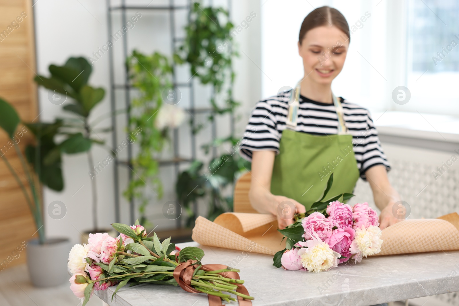 Florist making bouquet of peonies at table in flower shop, selective focus. Space for text Photo of Florist making bouquet of peonies at table in flower shop, selective focus. Space for text