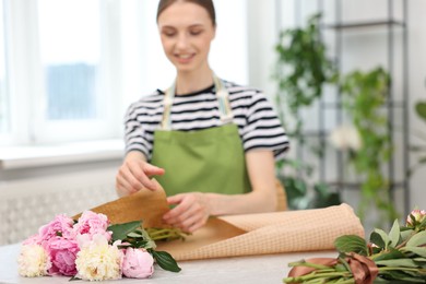 Photo of Florist making bouquet of peonies at table in flower shop, selective focus