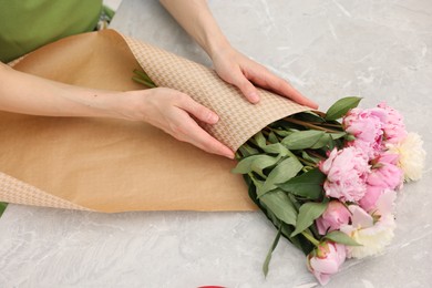 Photo of Florist making bouquet of peonies at grey marble table, above view