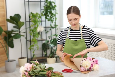 Photo of Florist making bouquet of peonies at table in flower shop, space for text