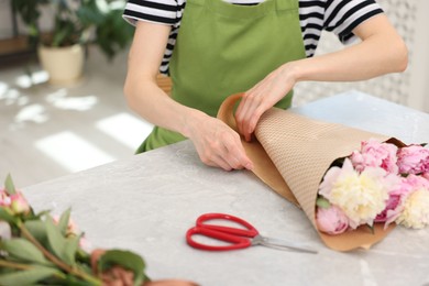 Photo of Florist making bouquet of peonies at grey marble table in flower shop, closeup