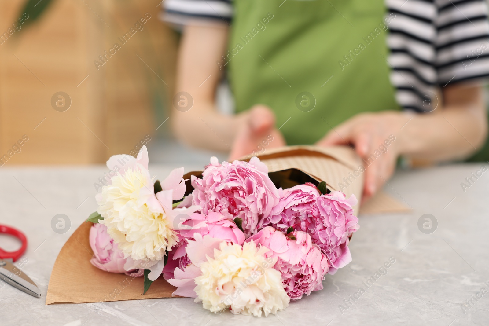 Florist making bouquet of peonies at grey marble table in flower shop, selective focus Photo of Florist making bouquet of peonies at grey marble table in flower shop, selective focus