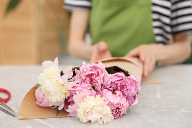 Photo of Florist making bouquet of peonies at grey marble table in flower shop, selective focus