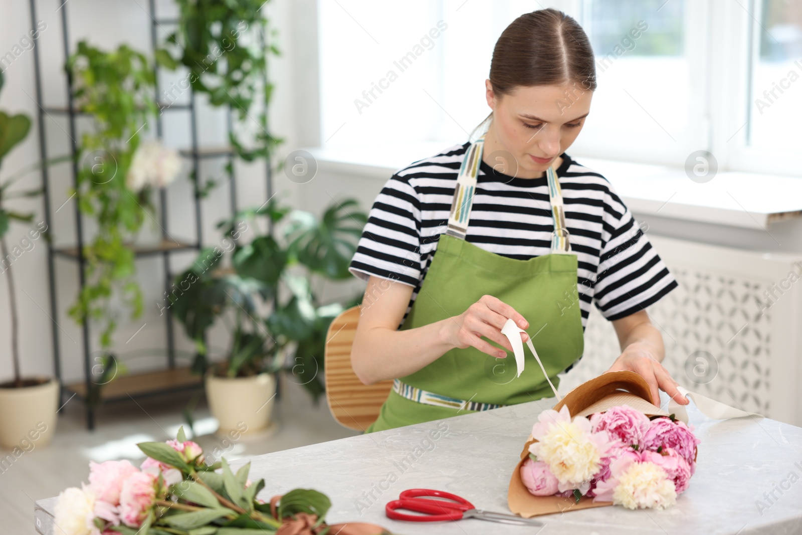 Florist making bouquet of peonies at table in flower shop, space for text Photo of Florist making bouquet of peonies at table in flower shop, space for text