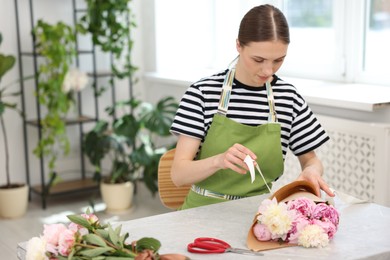 Photo of Florist making bouquet of peonies at table in flower shop, space for text