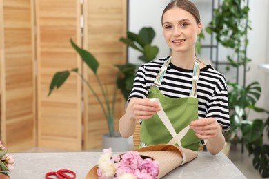 Photo of Florist making bouquet of peonies at table in flower shop, space for text