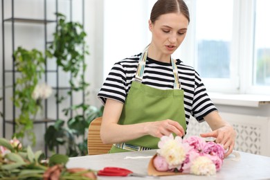 Photo of Florist making bouquet of peonies at table in flower shop, space for text