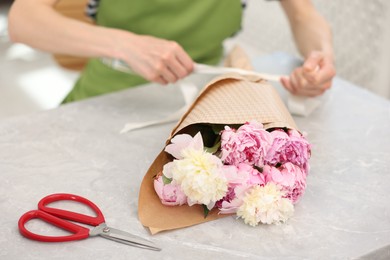 Photo of Florist making bouquet of peonies at grey marble table in flower shop, selective focus