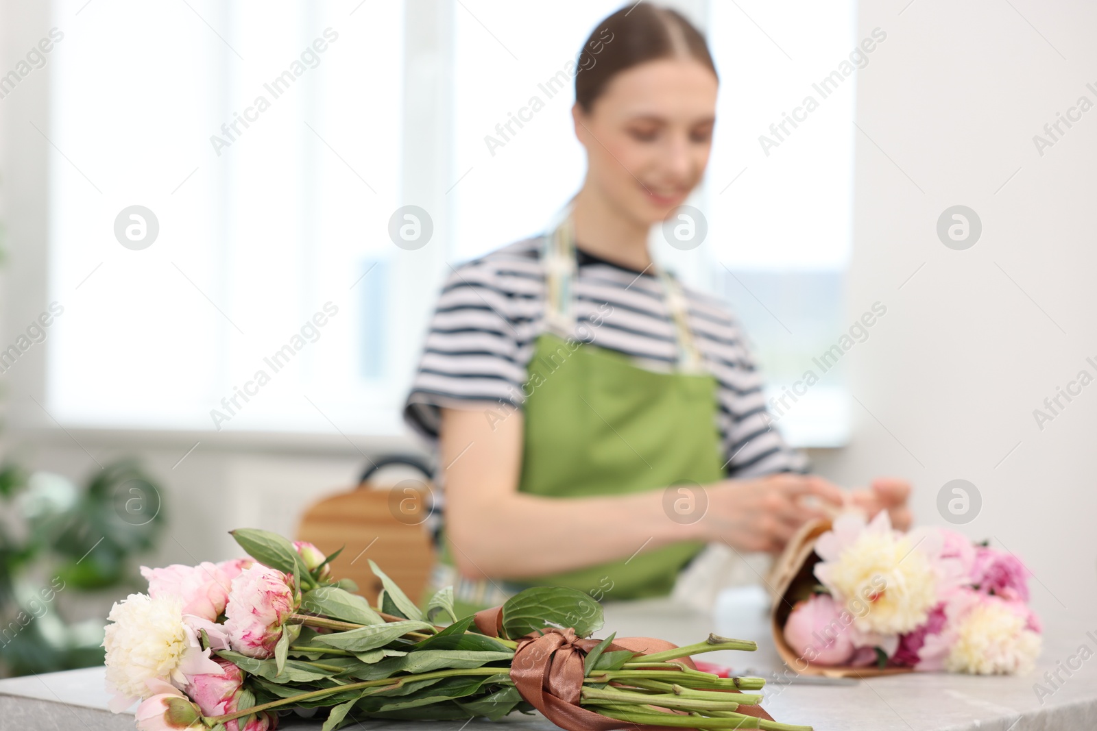 Florist making bouquet of peonies at table in flower shop, selective focus Photo of Florist making bouquet of peonies at table in flower shop, selective focus
