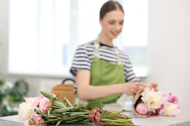 Photo of Florist making bouquet of peonies at table in flower shop, selective focus