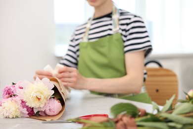 Photo of Florist making bouquet of peonies at table in flower shop, selective focus