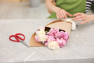 Photo of Florist making beautiful bouquet of peonies at grey marble table, selective focus
