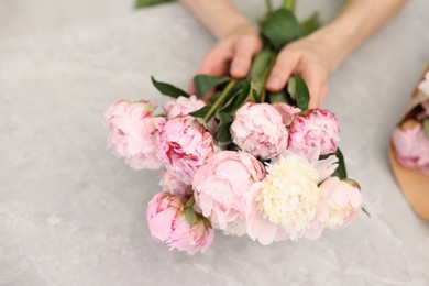 Photo of Florist making beautiful bouquet of peonies at grey marble table, closeup